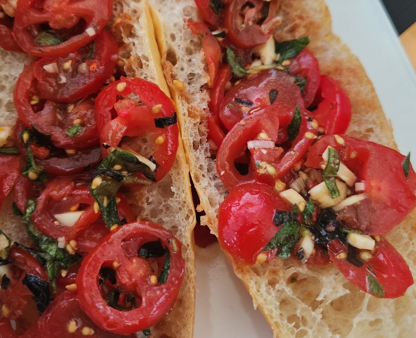 Two pieces of grilled bread piled with sliced tomato and rings of sweet pepper.