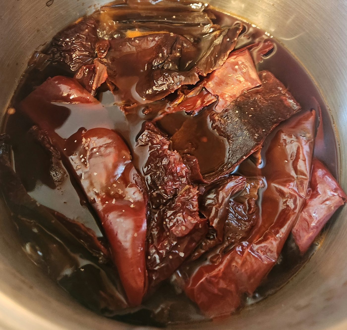 Dried chiles simmering in a steel pan of beef stock, the liquid gone deep red.