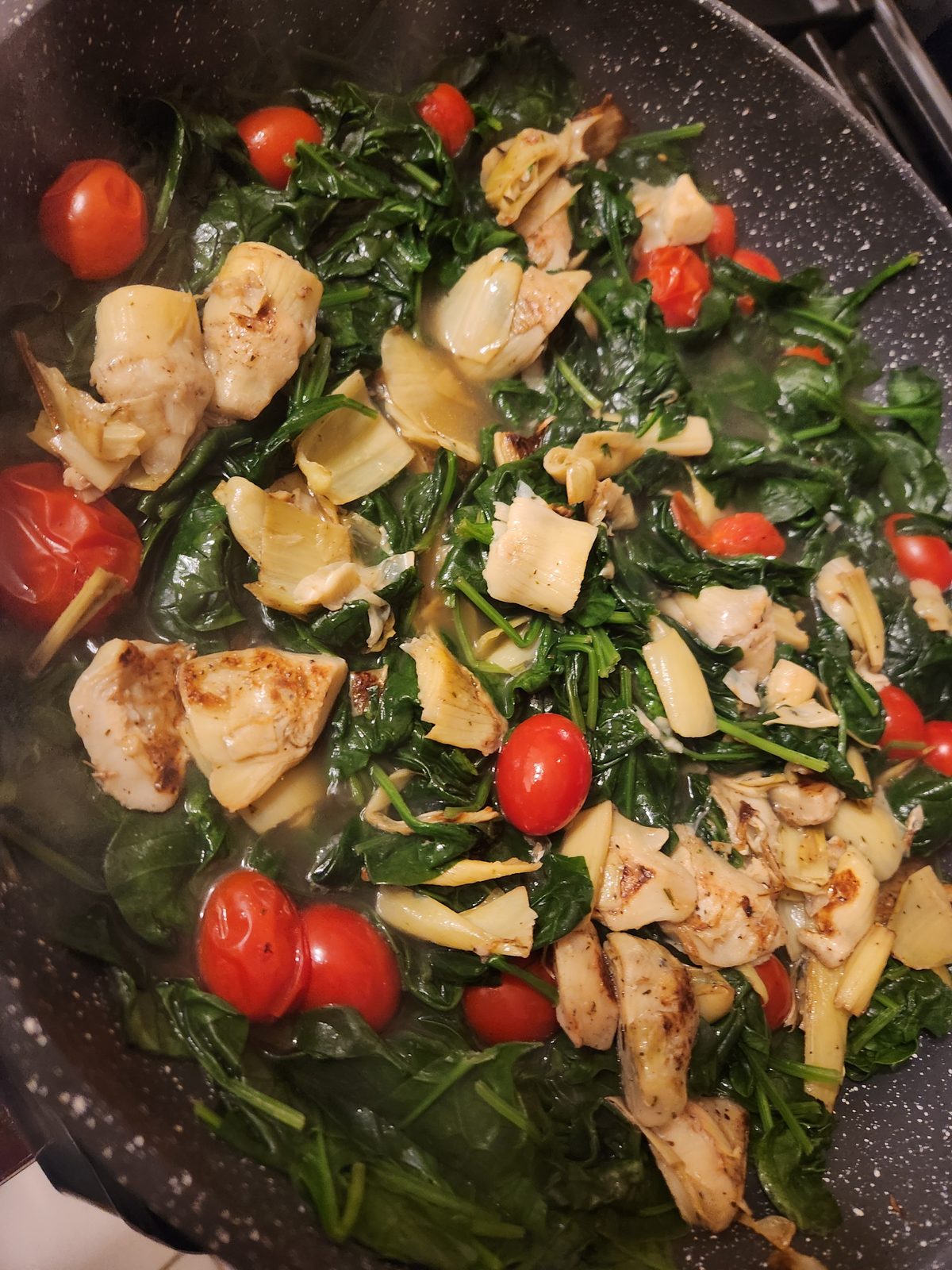 A pan of browned chicken pieces with wilted spinach and whole red cherry tomatoes.