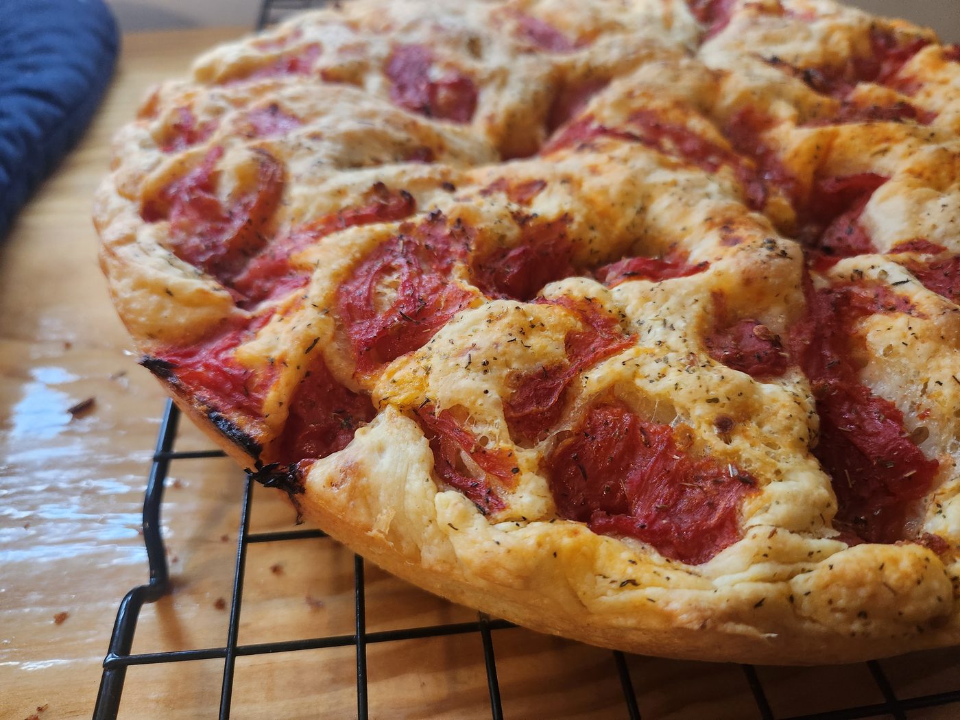 The same focaccia turned out onto a wire rack, showing a pale golden underside and a scorched patch at one edge of the rim.