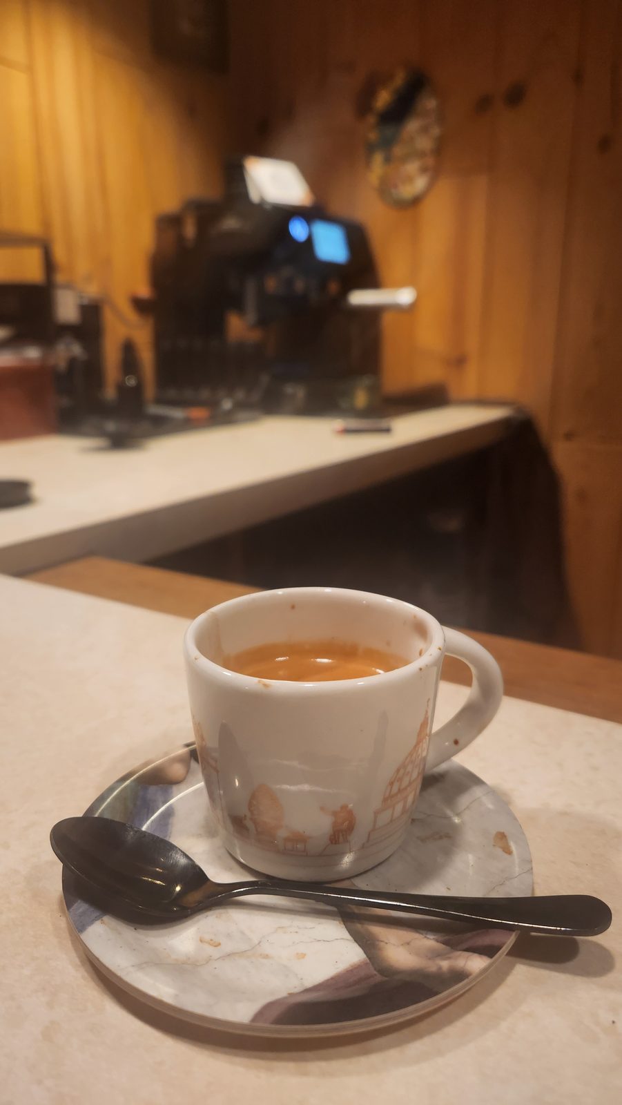 An empty espresso cup and spoon on a saucer beside the machine.