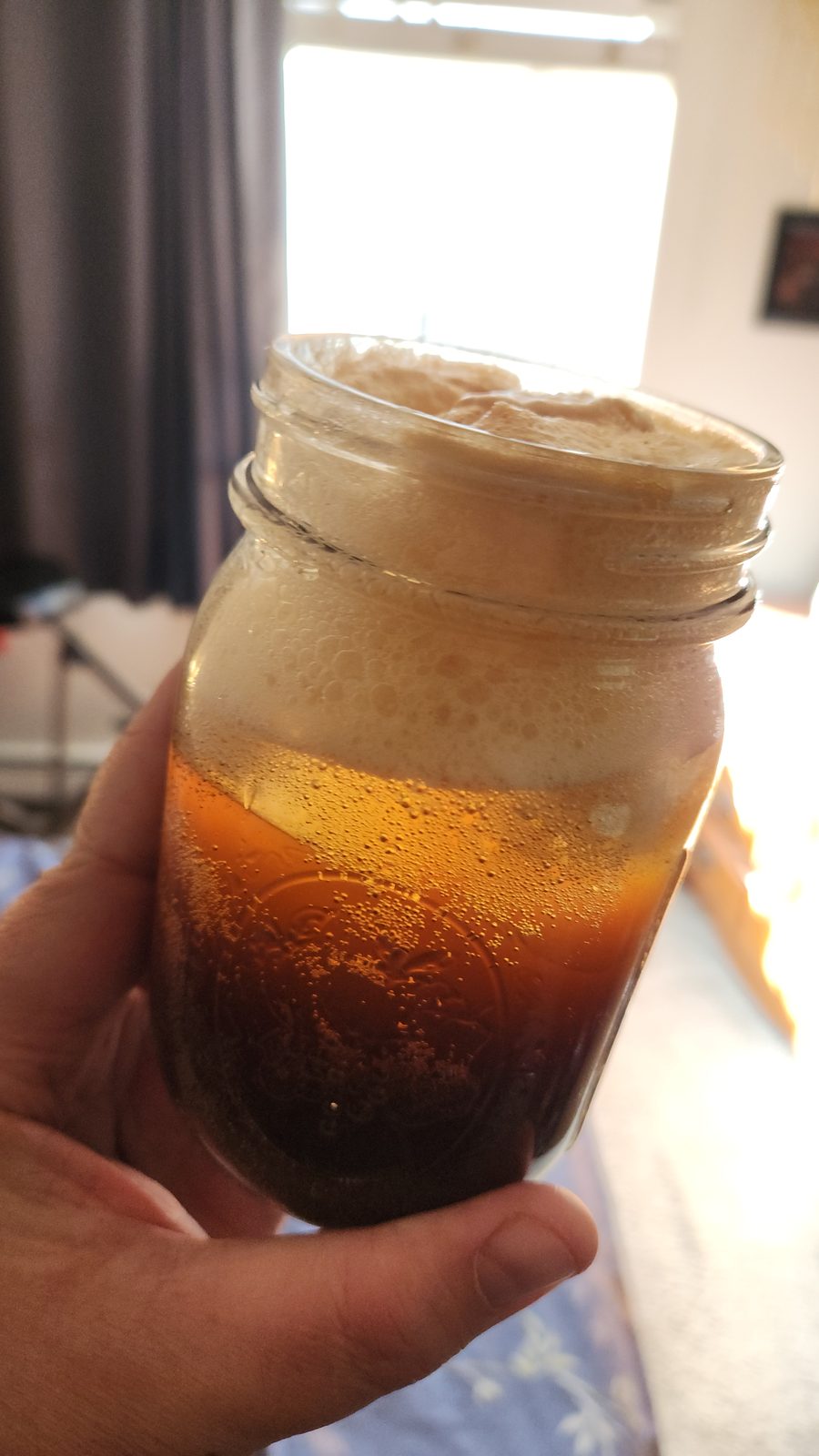 A jar of espresso tonic held to the light, the dark coffee layer sitting over pale tonic and ice.