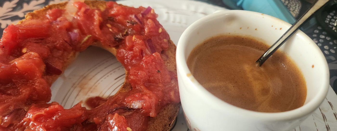 A frazzella topped with chopped tomato beside a cup of espresso on a white counter.