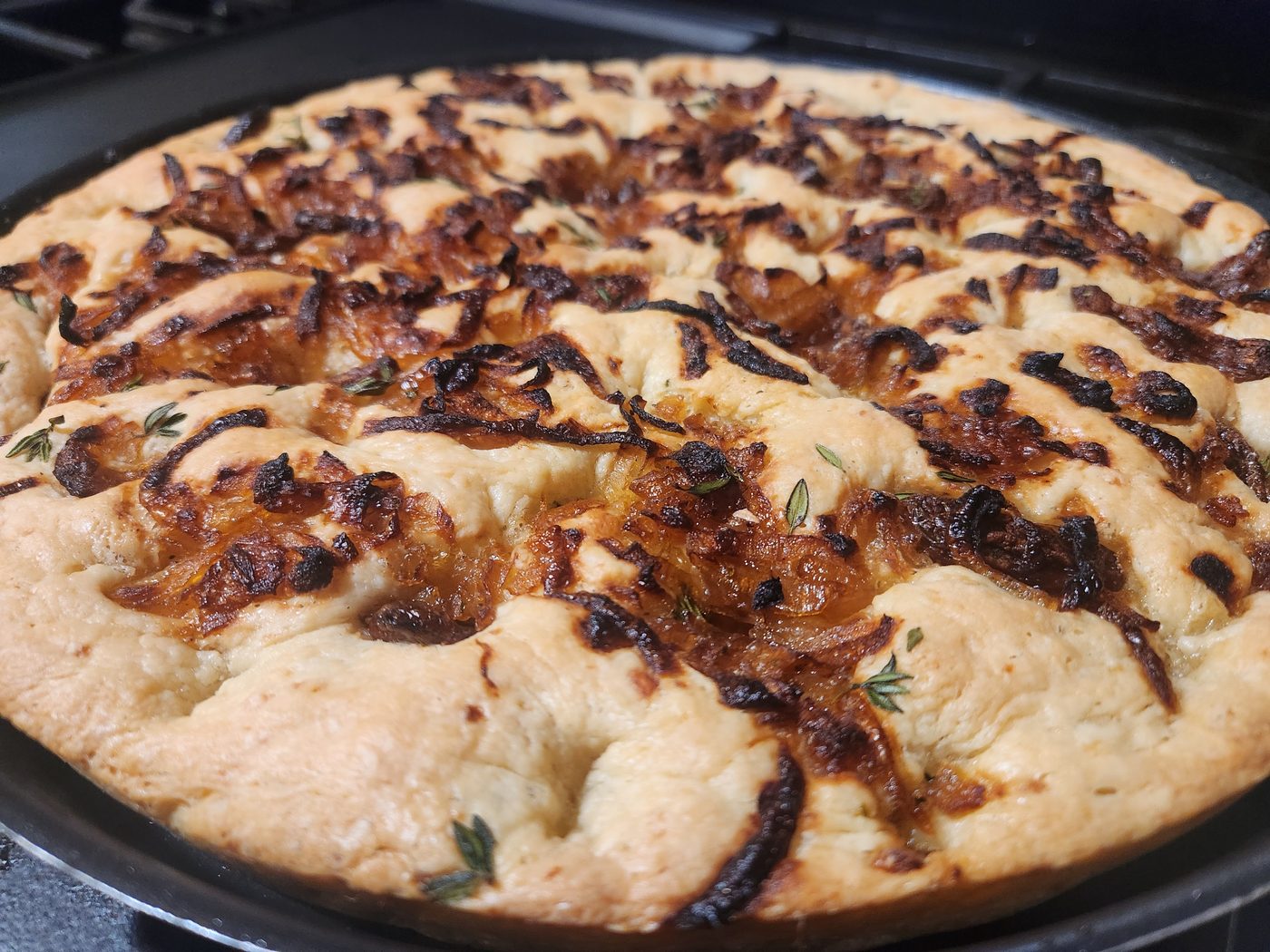 A round focaccia covered in dark caramelised onion and whole soft garlic cloves, scattered with thyme.